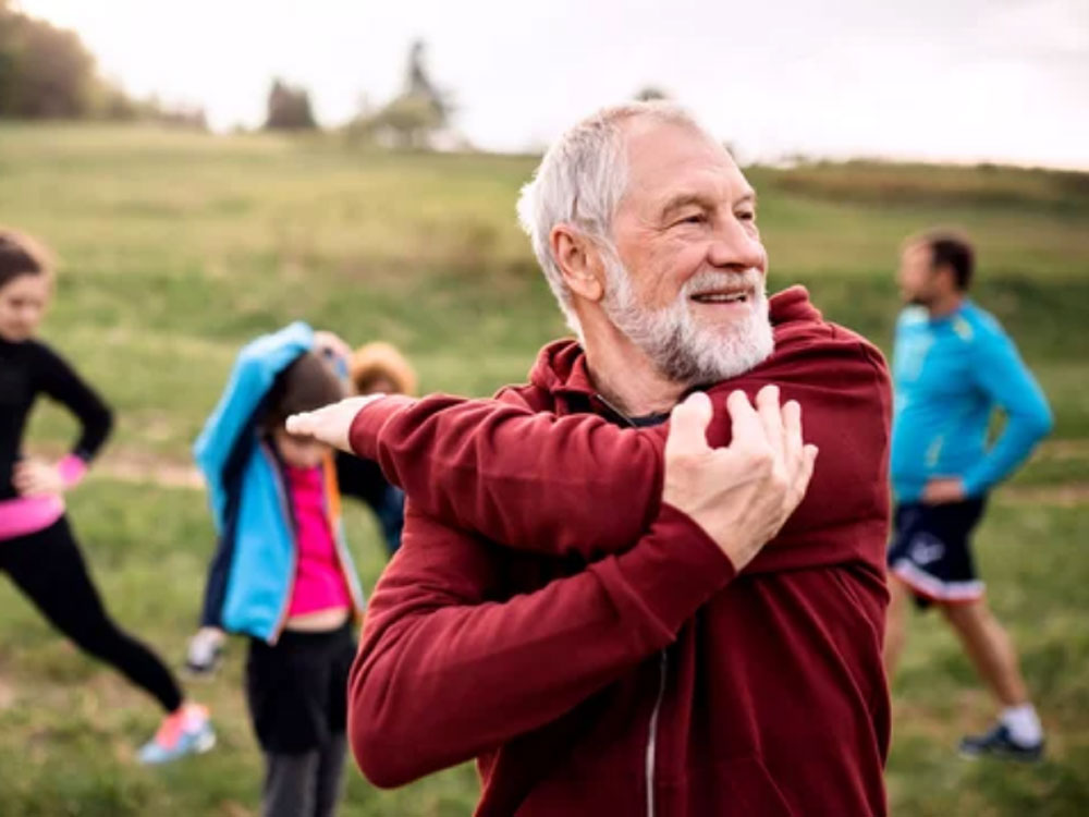 A smiling elderly man in front of a group of runners, ROC Orthopedics