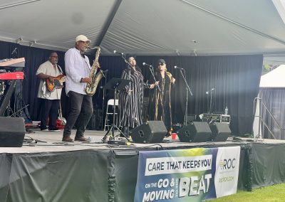 Band performing with a banner showing ROC sponsored the stage for 2025's Lake Oswego Arts Festival